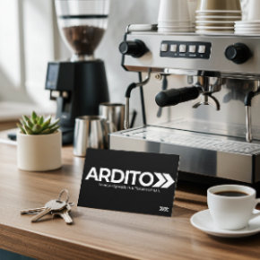 A close-up of a professional espresso machine on a wooden countertop, with a black business card displaying the brand 'ARDITO' gift card in the foreground, alongside coffee cups, a small potted succulent, and keys.
